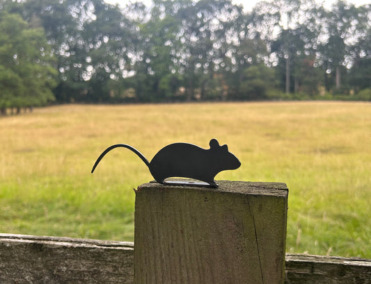 Black silhouette of a mouse on a wooden post with a field and trees in the background
