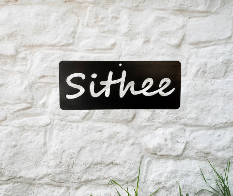 Metal sign with 'Sithee' text on a textured white wall.