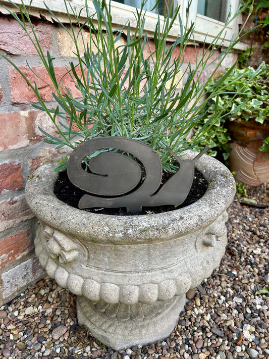 Decorative stone urn with a metal snail sculpture and plants against a brick wall.