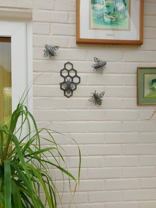 a display of metal 3D Bee's and honeycomb on a brick wall surrounded by plants and pictures