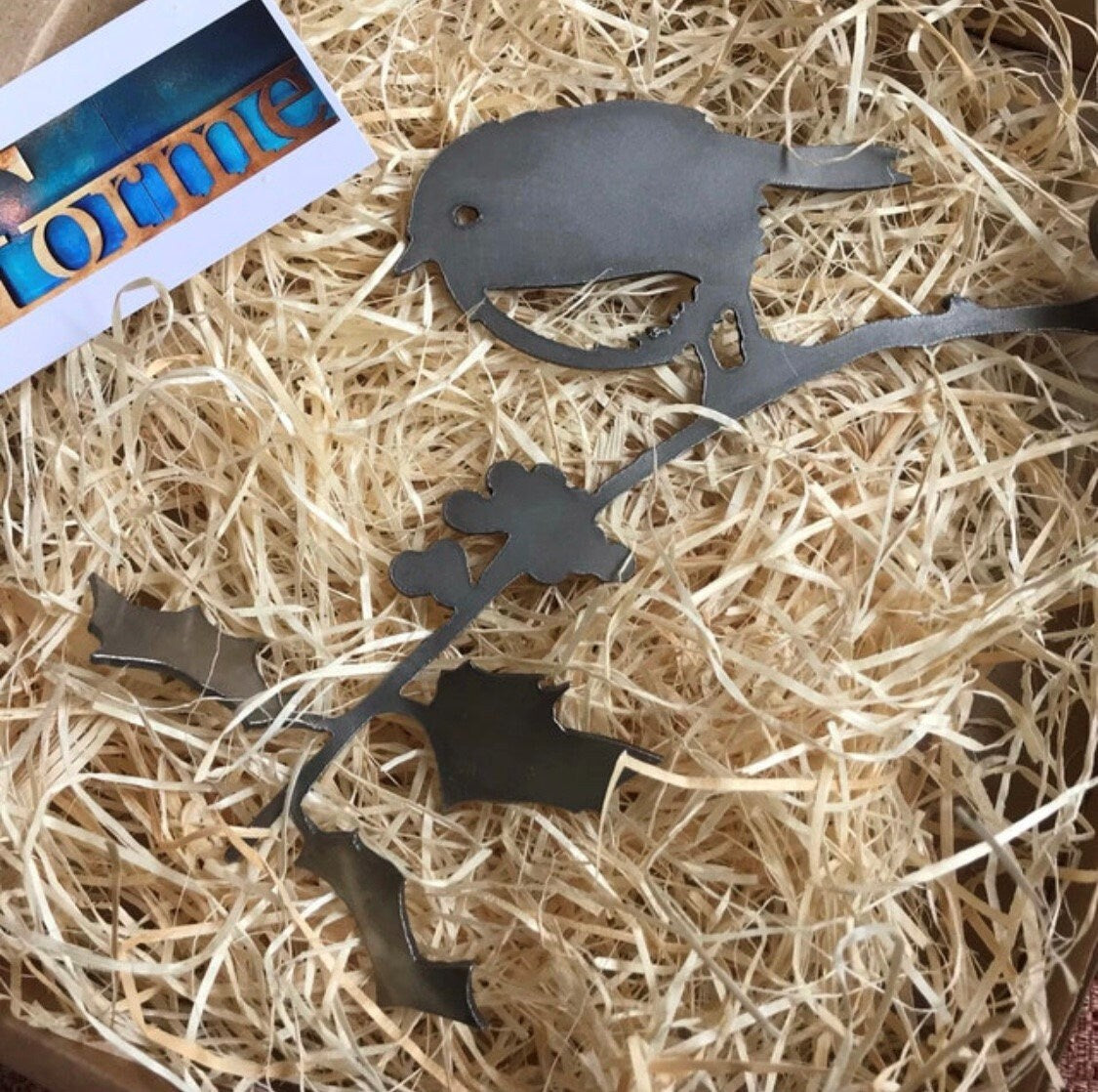 Steel Robin on a Holly Branch on a bed of wood wool, eco-friendly packaging with a Forme Steel Business Card.