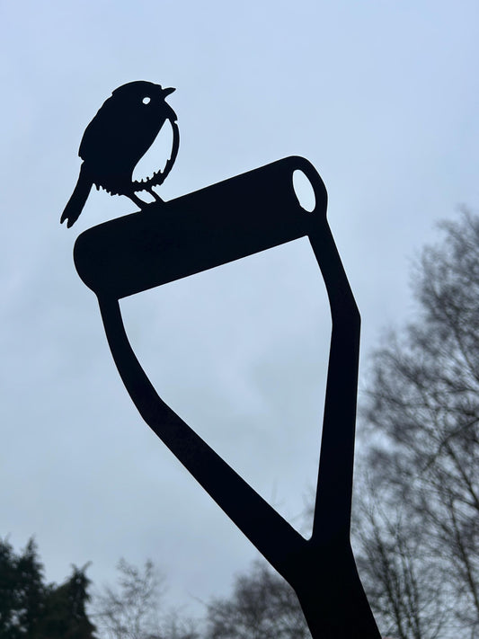 Silhouette of a steel robin garden ornament, sat on the handle of a garden spade.