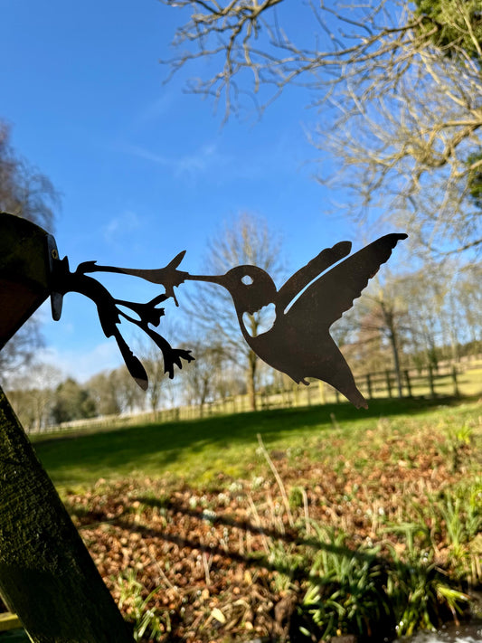 Steel Hummingbird Garden decoration mounted to a fence with trees in the background