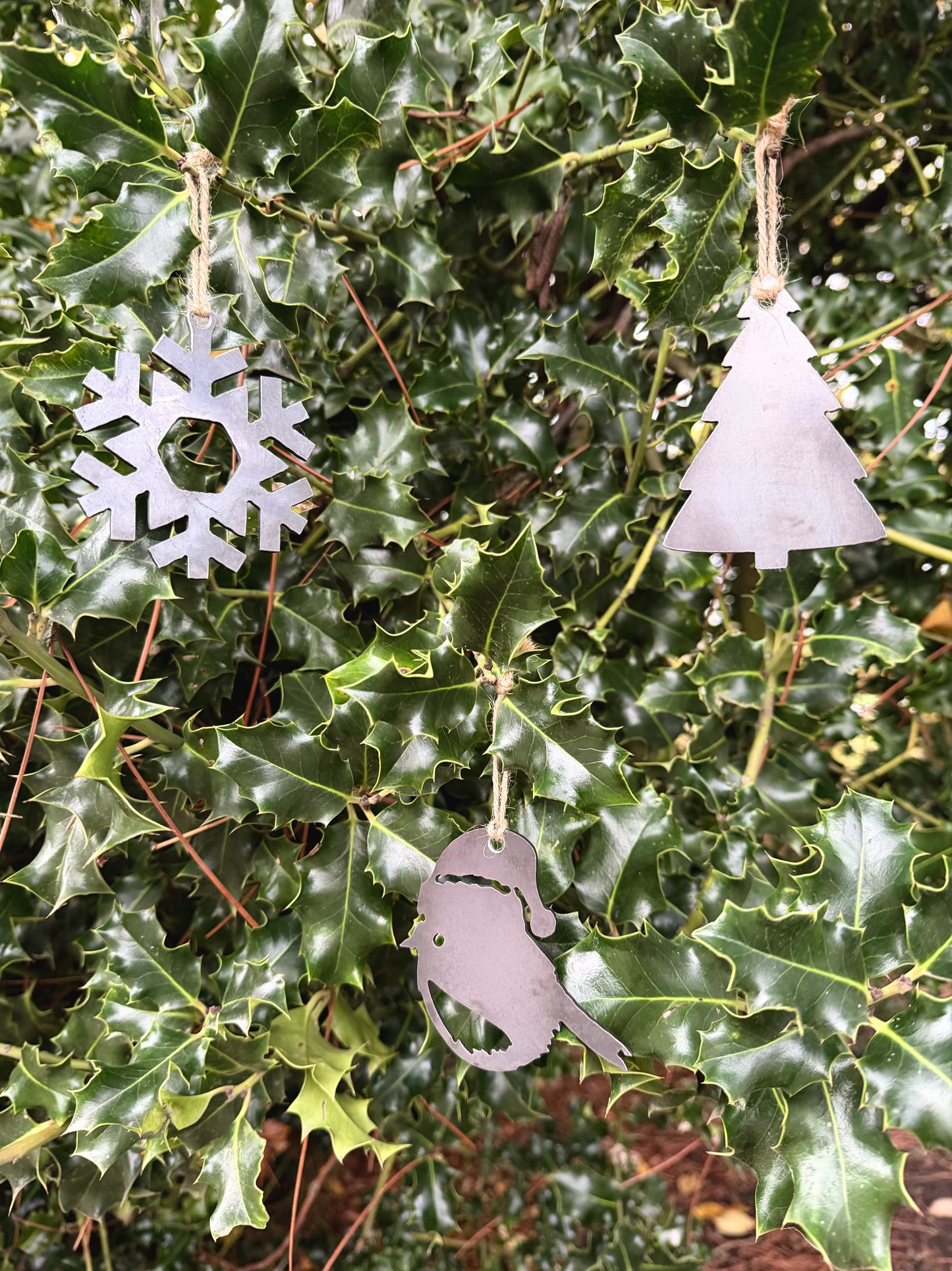 Metal Christmas tree decorations hanging on green holly leaves. Snowflake, Robin and Christmas Tree.