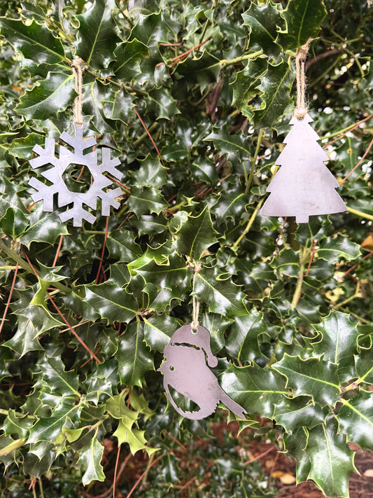 Metal Christmas tree decorations hanging on green holly leaves. Snowflake, Robin and Christmas Tree.