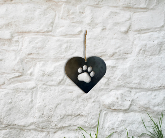 Steel Love Heart with Paw Print Cut Out hanging by a piece of string against a white brick wall. 
