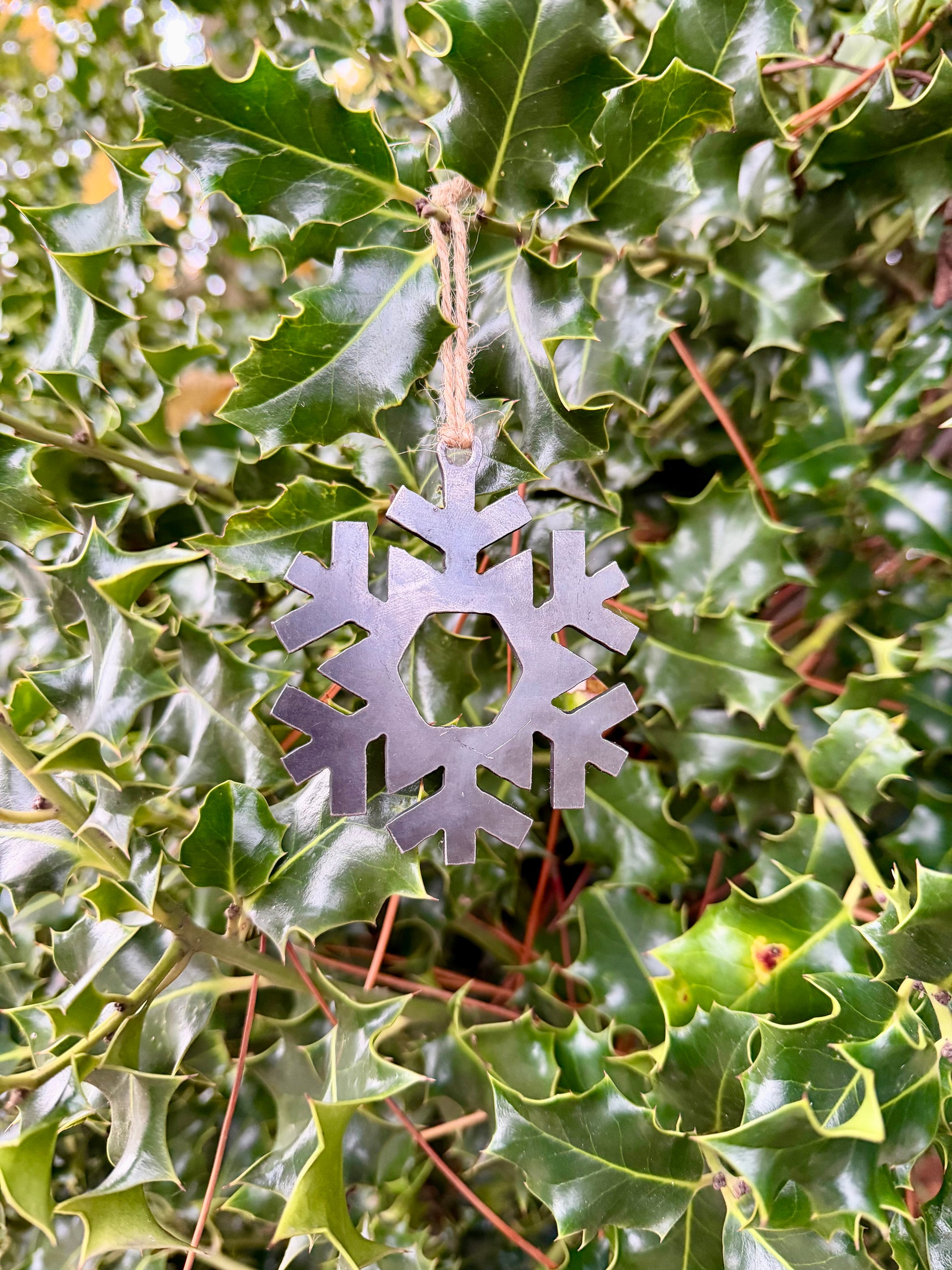 Metal snowflake decoration hanging on green holly leaves