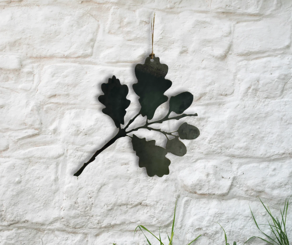 Decorative metal oak leaf wall art on a textured white stone wall.