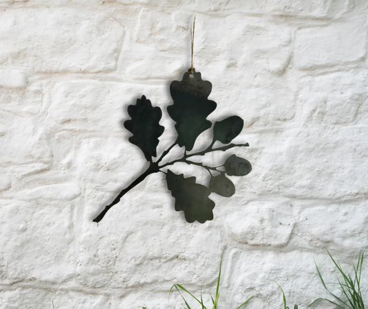 Decorative metal oak leaf wall art on a textured white stone wall.