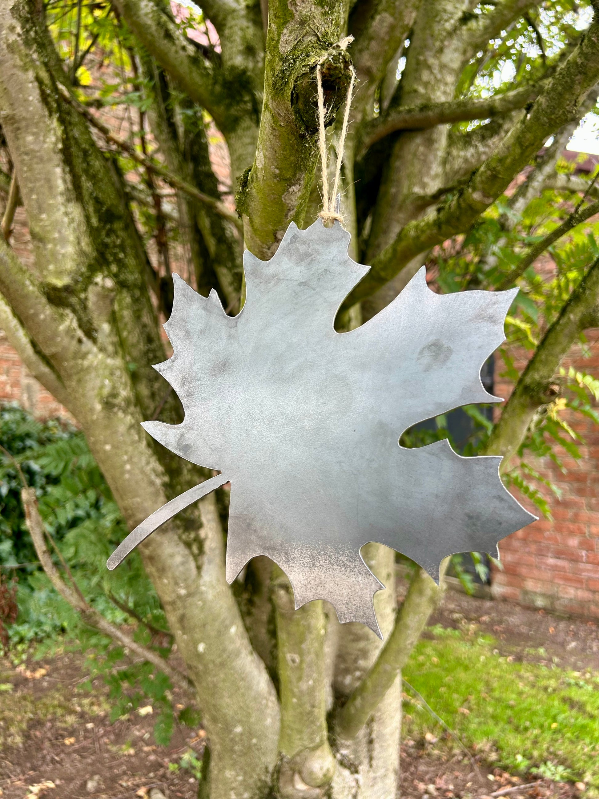 Decorative metal maple leaf ornament hanging from a tree