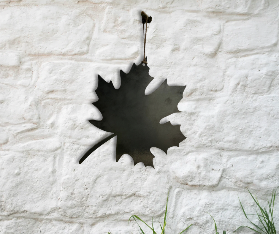 Decorative metal maple leaf ornament on white brick wall
