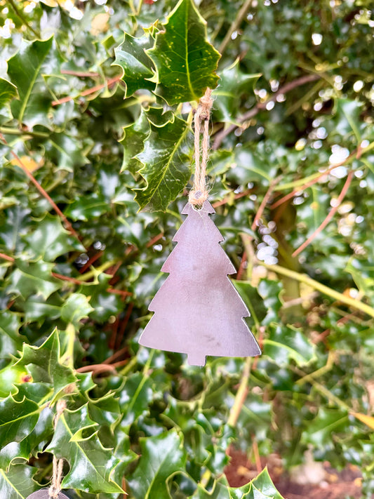 Metal Christmas tree decoration hanging on green holly leaves