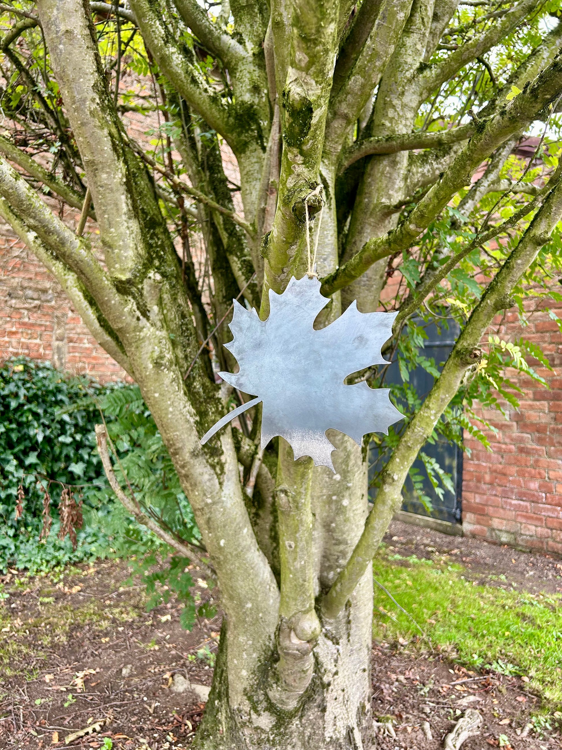 Decorative metal maple leaf ornament hanging from a tree