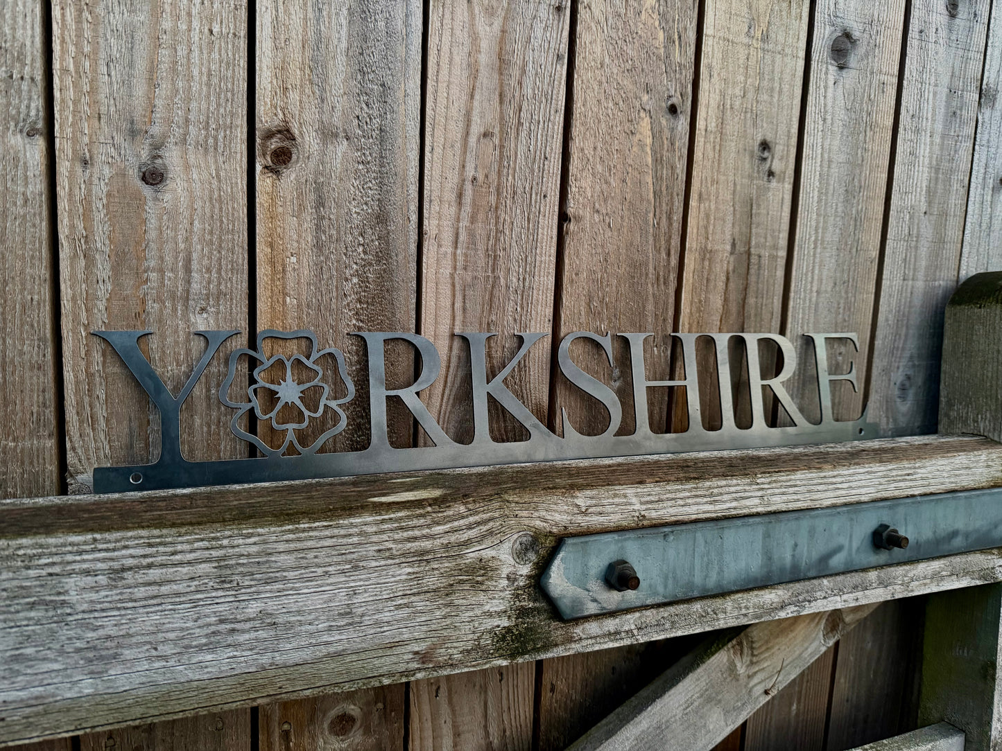 Hand holding a 'Yorkshire' sign with the 'o' replaced with a Yorkshire Rose, against a wooden background