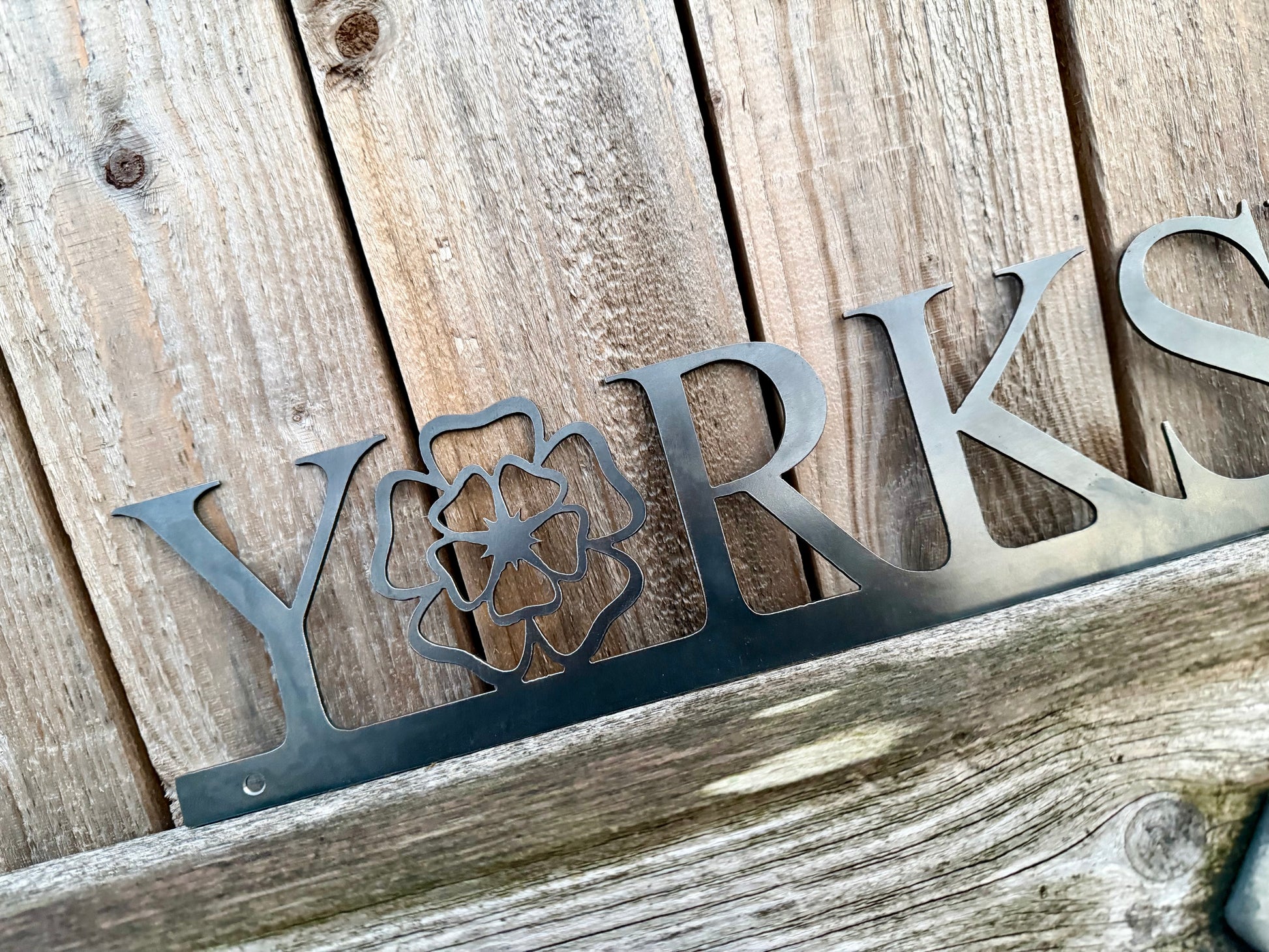 Hand holding a 'Yorkshire' sign with the 'o' replaced with a Yorkshire Rose, against a wooden background