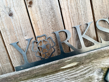 Hand holding a 'Yorkshire' sign with the 'o' replaced with a Yorkshire Rose, against a wooden background