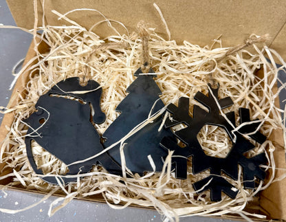 Three black Christmas-themed decorations, snowflake, Robin and Christmas Tree nestled in a boxed lined with wood shavings.