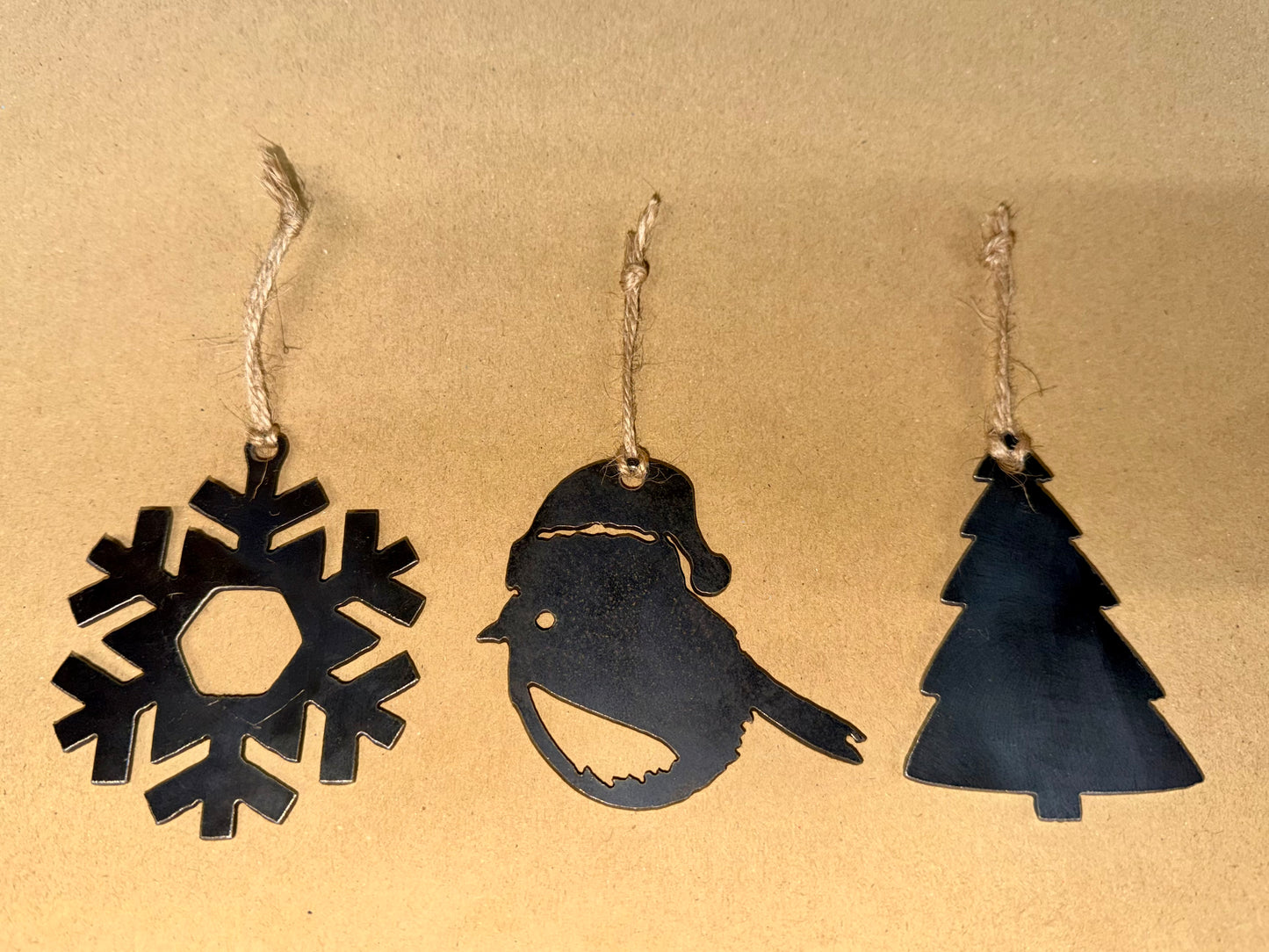 Three black Christmas-themed decorations, snowflake, Robin and Christmas Tree on a beige background