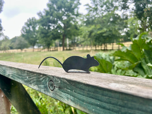 Black mouse silhouette on a wooden railing with a green field and trees in the background