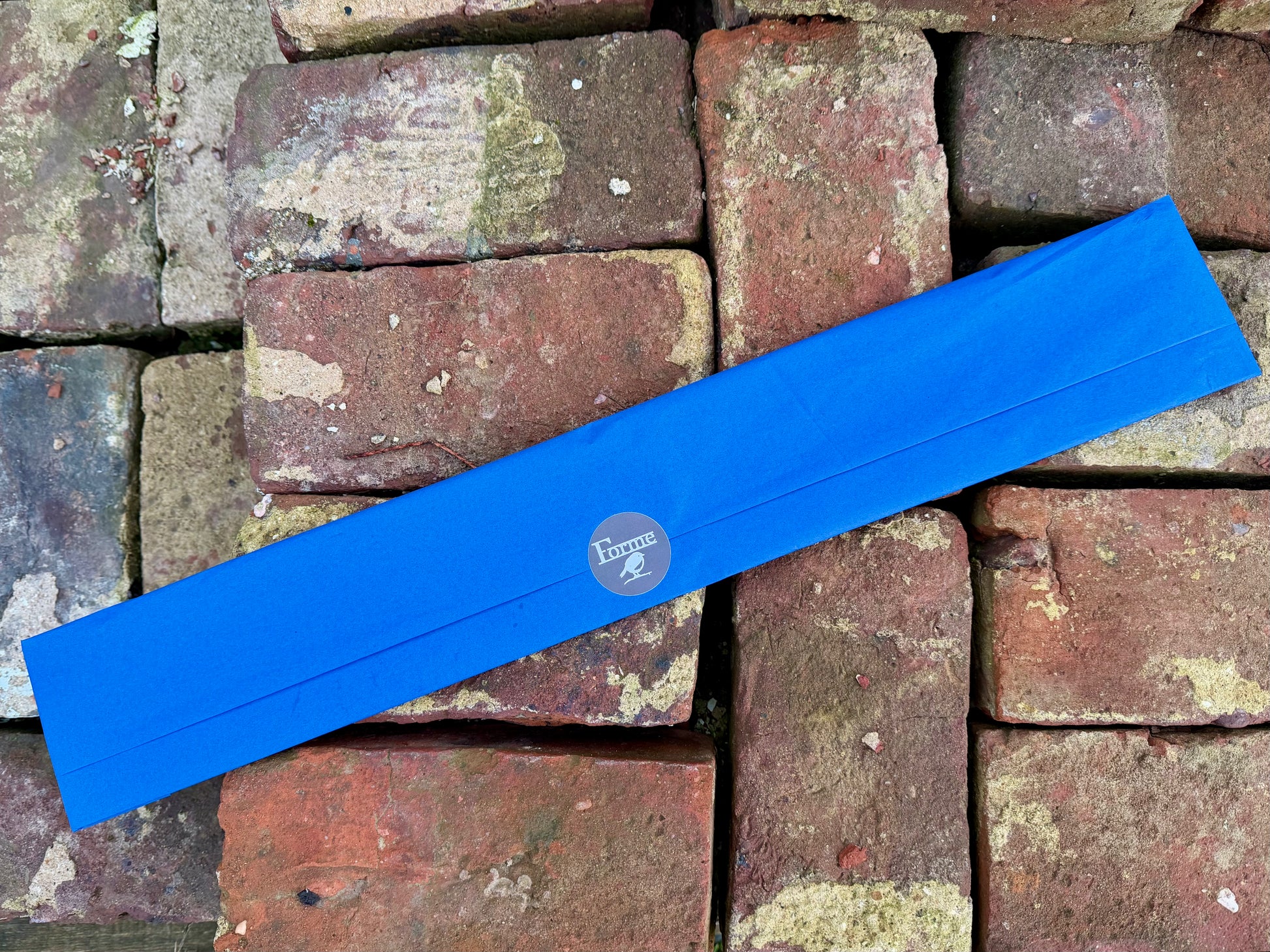 A product gift wrapped in blue tissue paper sealed with a branded Forme sticker displayed on a stack of bricks
