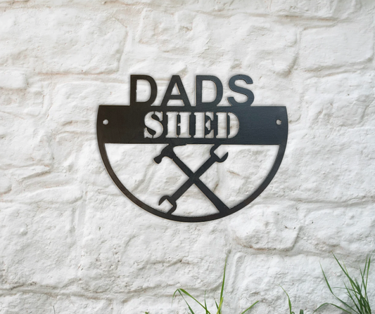 Metal sign with 'DADS SHED' text on a stone wall background