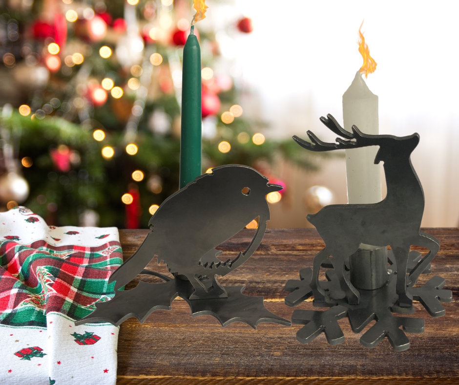Decorative candle holders shaped like a Rpbin and a reindeer on a wooden surface with a Christmas tree in the background.